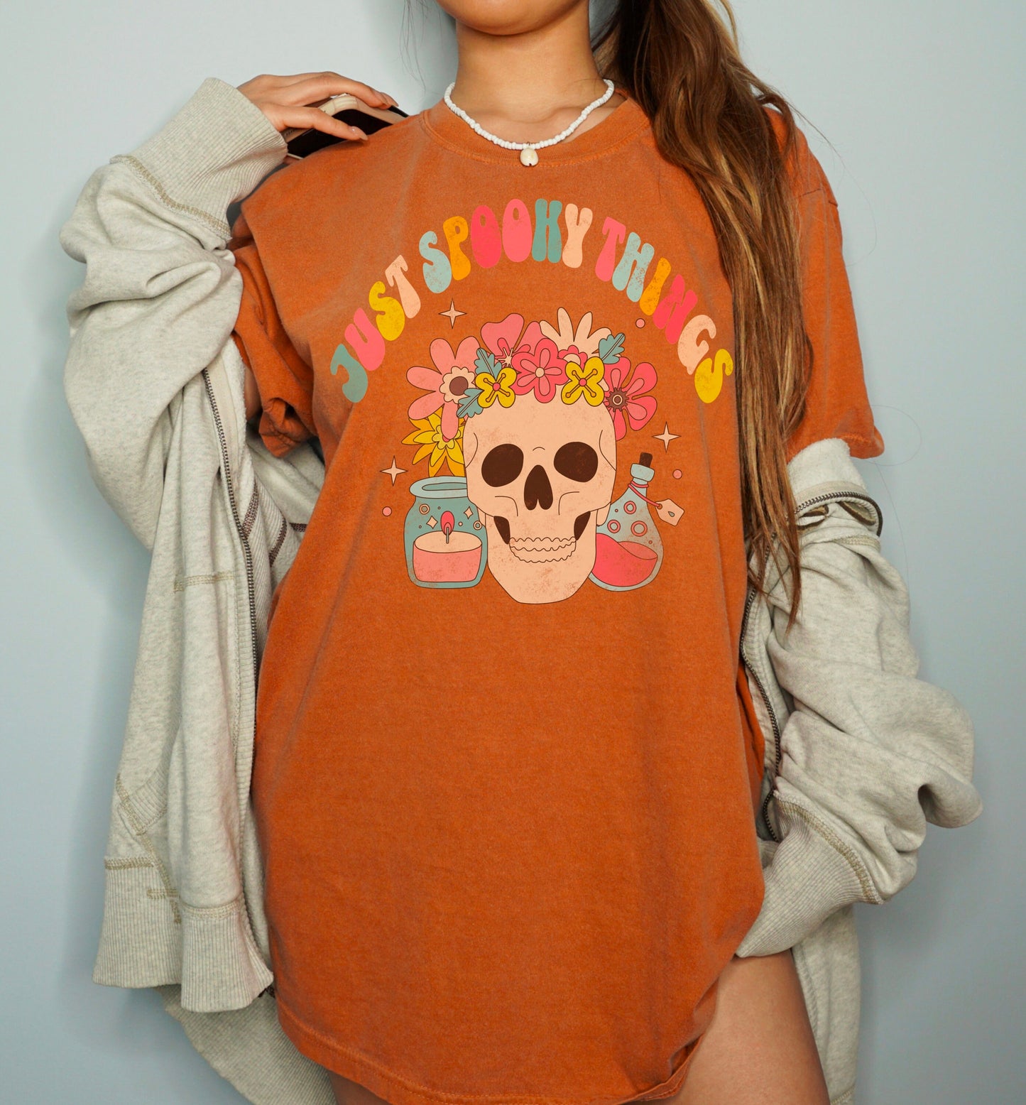 A t shirt in the color &quot;Yam&quot; with the words &quot;Just Spooky Things&quot; in Multicolor Retro Letters. Design features a skull with a flower crown, a candle, and a bottle of potion.