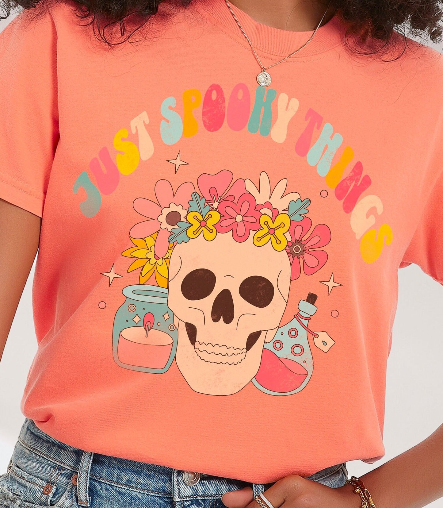 A t shirt in the color &quot;Terracotta&quot; with the words &quot;Just Spooky Things&quot; in Multicolor Retro Letters. Design features a skull with a flower crown, a candle, and a bottle of potion.