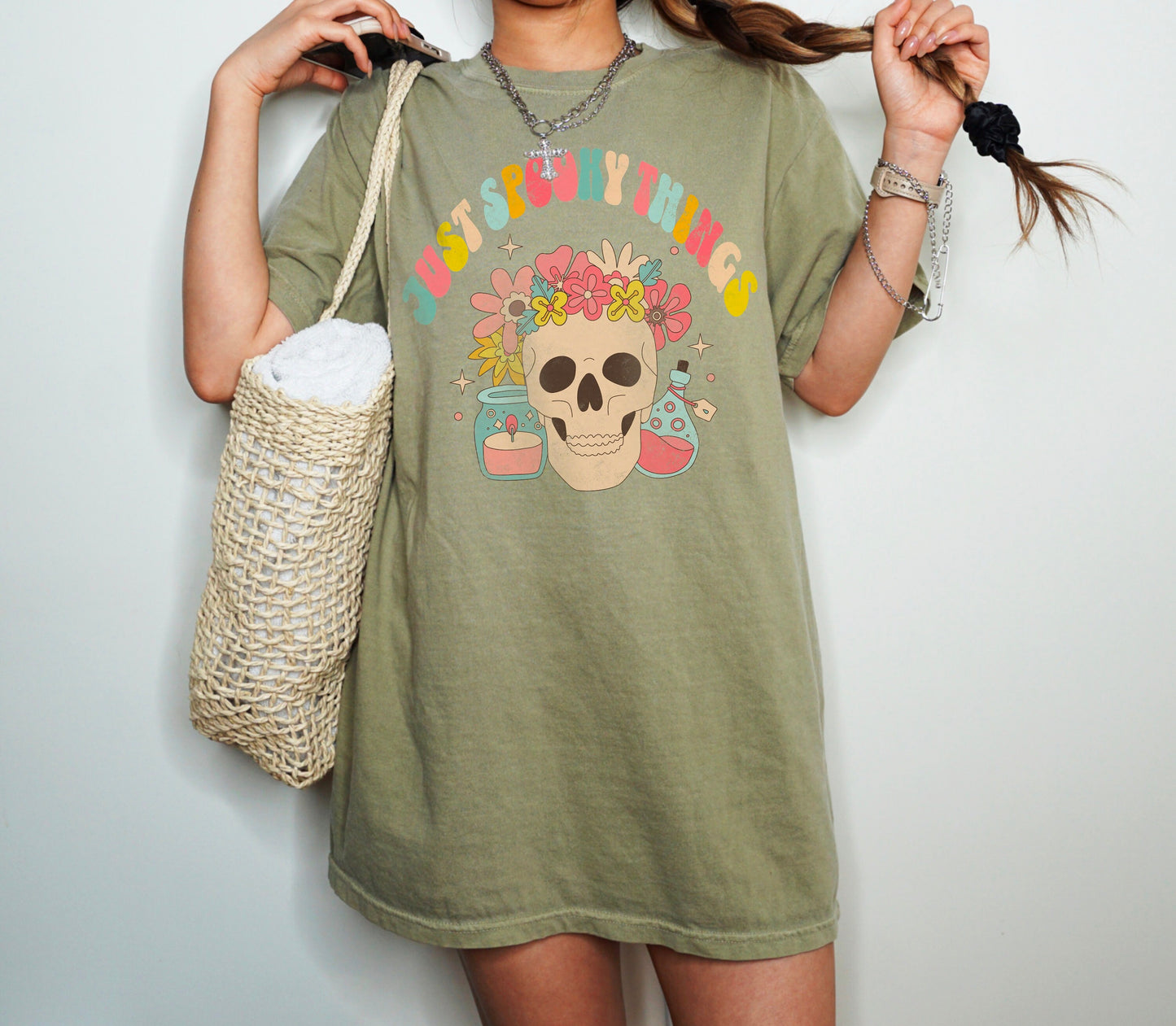 A t shirt in the color &quot;Khaki&quot; with the words &quot;Just Spooky Things&quot; in Multicolor Retro Letters. Design features a skull with a flower crown, a candle, and a bottle of potion.