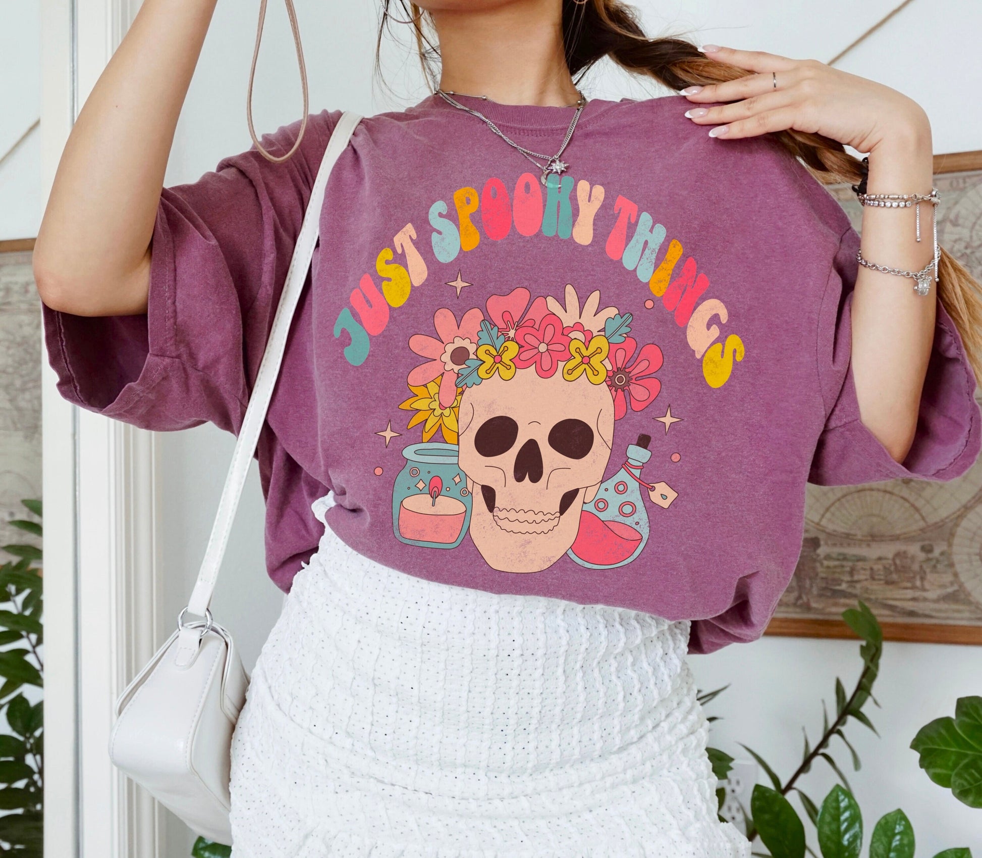 A t shirt in the color &quot;Berry&quot; with the words &quot;Just Spooky Things&quot; in Multicolor Retro Letters. Design features a skull with a flower crown, a candle, and a bottle of potion.